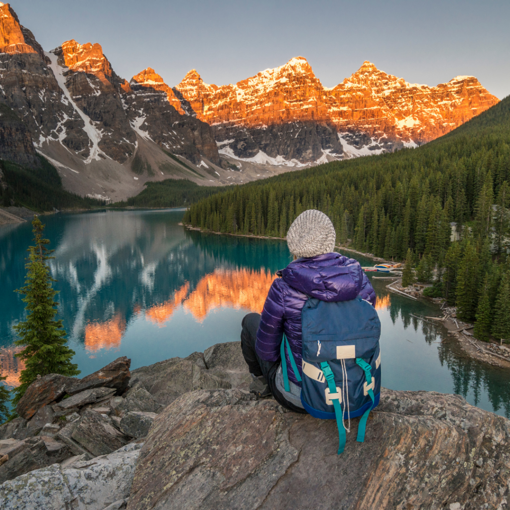A person sitting in front of a lake with mountains around it.