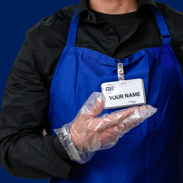man with a bright blue apron and black shirt pointing at his nametag. The nametag has the logo of CDS and the words "your name" on it. The man is wearing disposable food handling gloves.