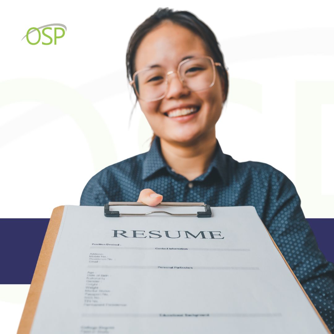 Young asian woman with glasses handing a clipboard with a resume on it towards the camera
